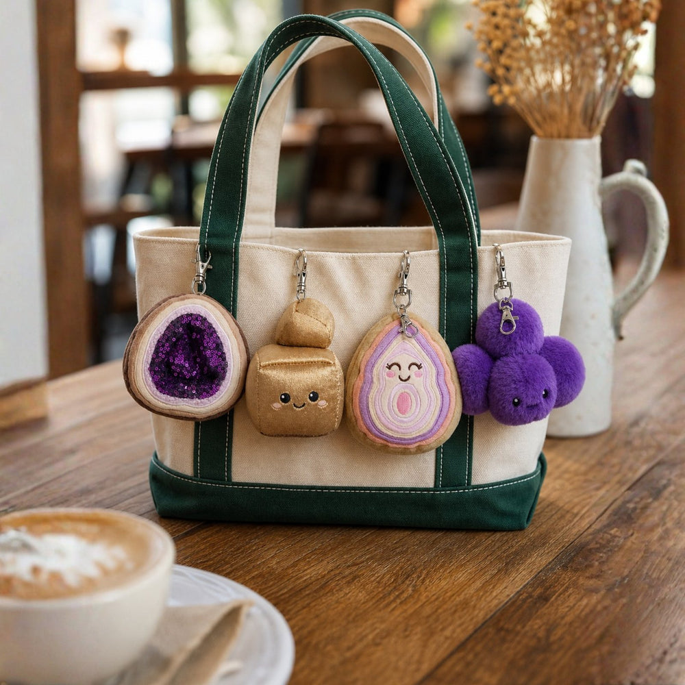 Four Crystal Plushie bag charms clipped to a canvas tote on a cafe table