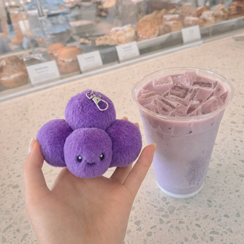 A hand holding Boba, the purple grape agate bag charm, beside an iced latte