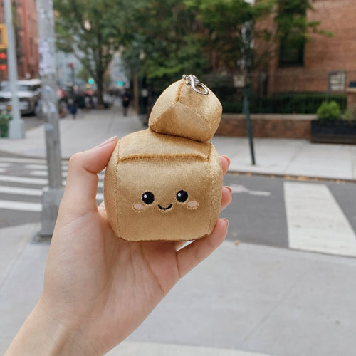 A hand holding Sparky, the gold pyrite bag charm, on a city sidewalk