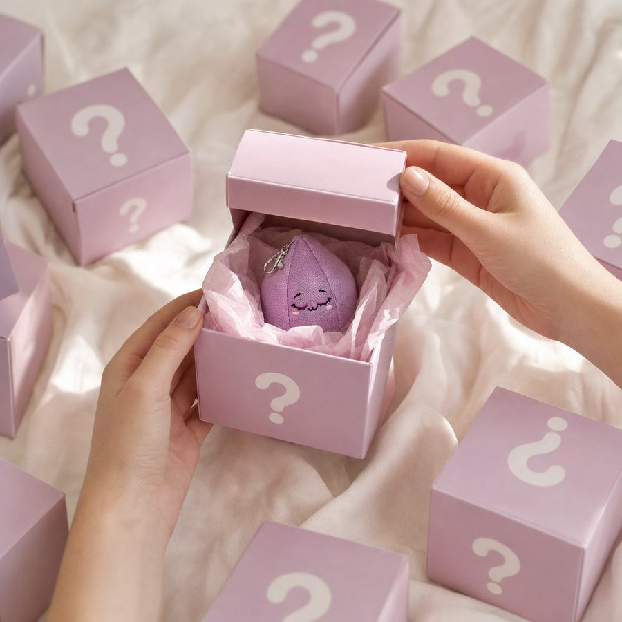 Hands opening a pastel mystery box with Baby Amy peeking out