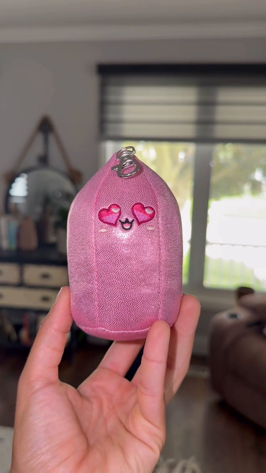 A hand holding Baby Rosie, the pink rose quartz bag charm with heart eyes